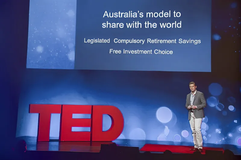 Nathan Ide presenting on the TED stage beside a slide on Australia's retirement savings model